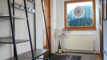 A modern room with a black metal shelving unit, a wooden door, a window with a view of greenery, and a radiator.