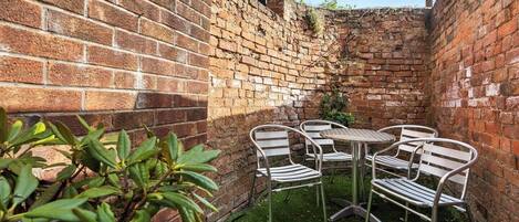 Pared de ladrillo con un pequeño jardín que incluye una mesa y sillas.