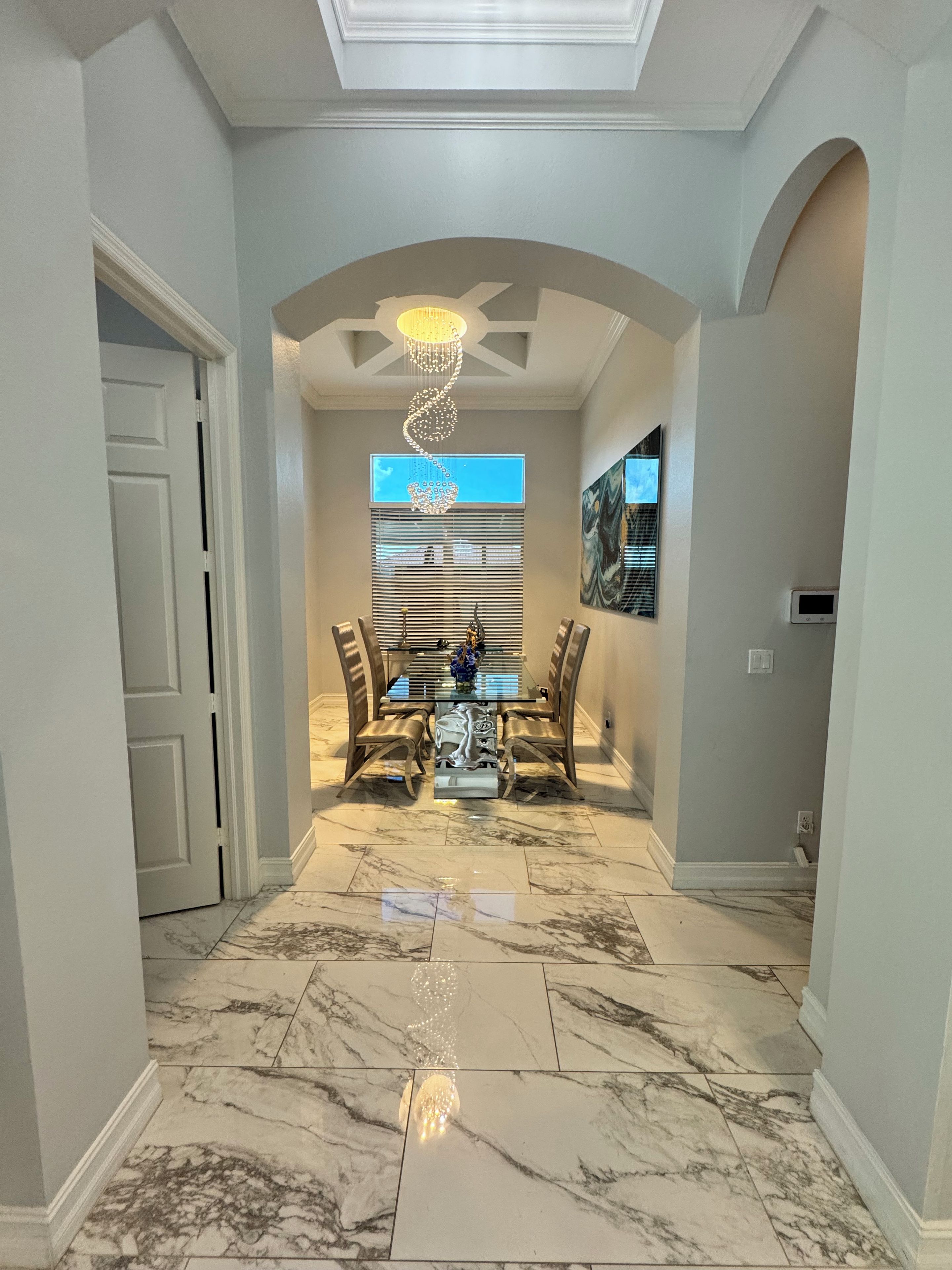 A hallway with a dining area featuring a glass table, chairs, and a chandelier.