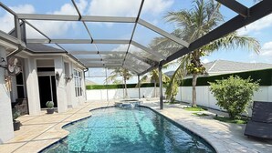Une piscine à bord incurvé, entourée d’un patio couvert doté d’une structure de toit en métal.