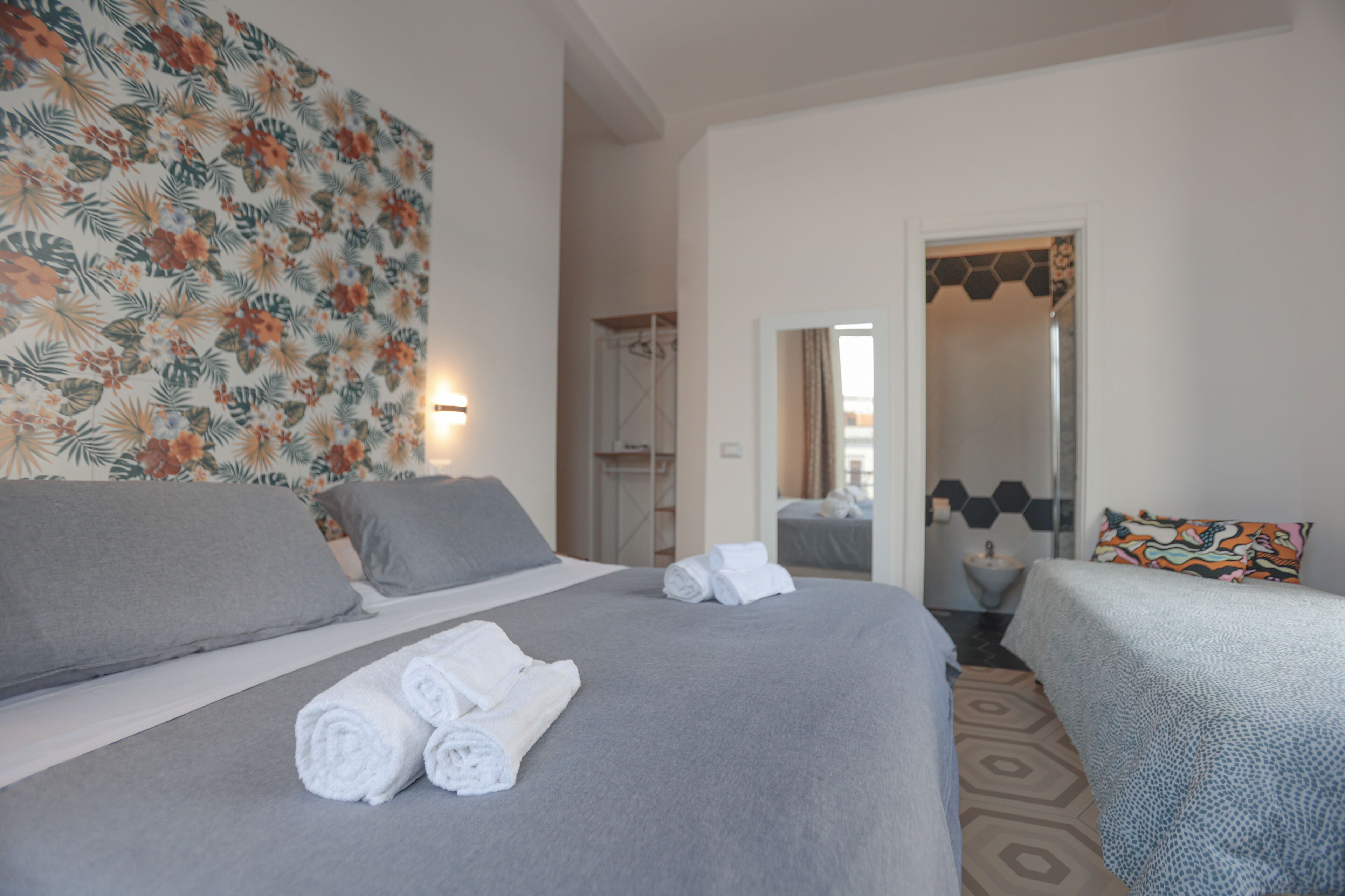 A hotel room with a large bed, two smaller beds, a shower area, and a bathroom with a mirror.