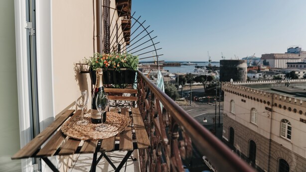 A balcony with a wooden table, a bottle of wine, and a potted plant. - DOMUS MARINA Rooms (Naples)