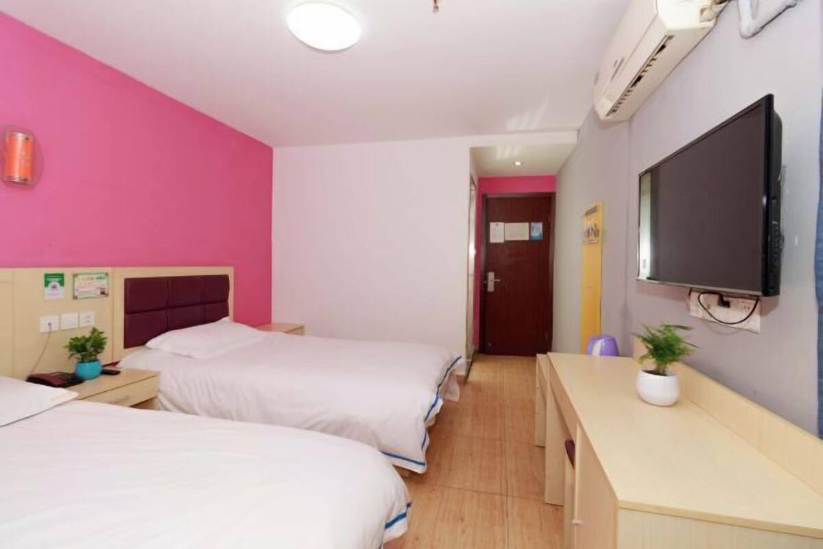 A hotel room with two beds, a desk, a TV, and an air conditioning unit.