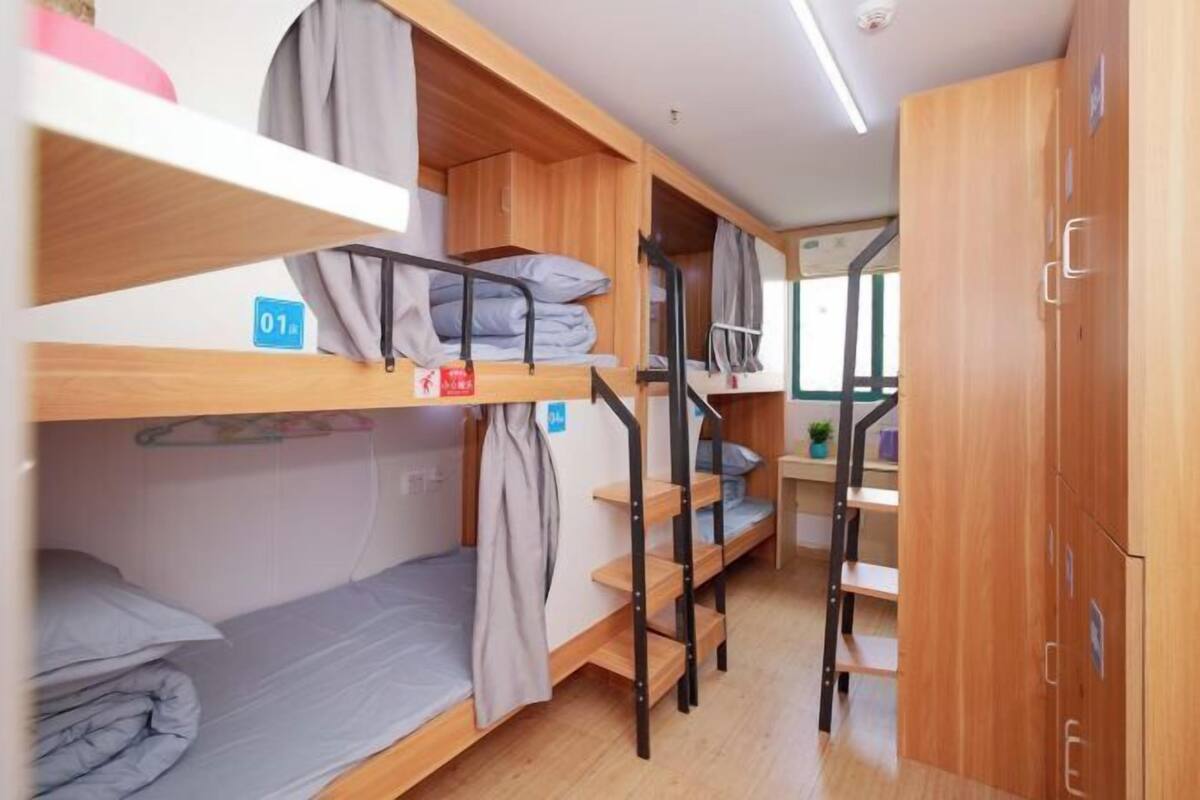 A dormitory room with bunk beds, a desk, and a wardrobe.
