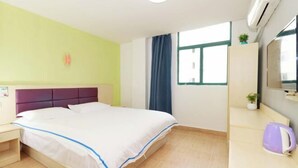 Una habitación de hotel con una cama, una mesita de noche, un escritorio pequeño con una silla, una ventana con cortinas y un aire acondicionado de pared.