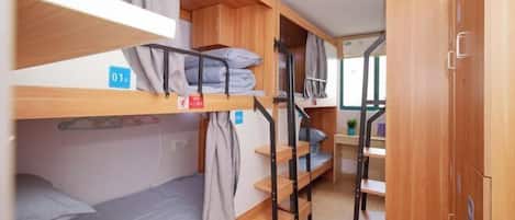 A dormitory room with bunk beds, wooden cabinets, and a small desk with a plant.