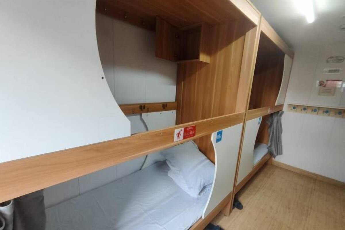 A bunk bed room with wooden headboards, a small cabinet, and a wall-mounted shelf.