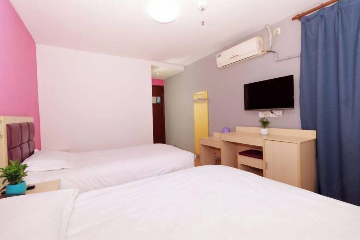 A hotel room with two beds, a desk, a chair, a TV, and an air conditioning unit.