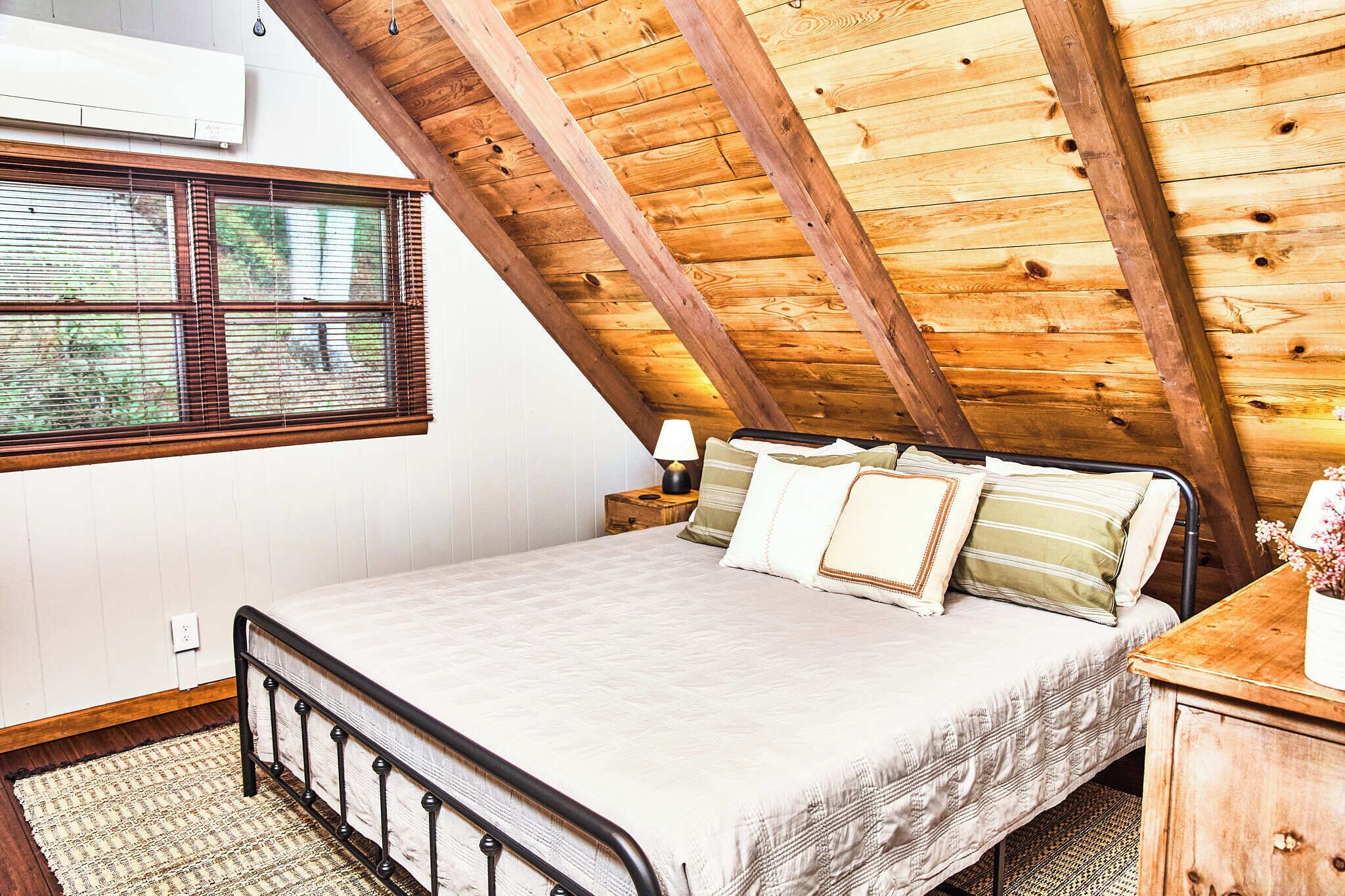 Een slaapkamer met een schuine kap, een bed, een nachtkastje en een raam met jaloezieën.