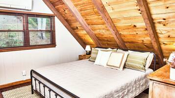Een slaapkamer met een schuine kap, een bed, een nachtkastje en een raam met jaloezieën.