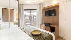 A hotel room with a bed, a desk, a television, and a view of the cityscape. - ARK Houses - Flat Standard Vista-Mar c/ Piscina na Cobertura (Santos)