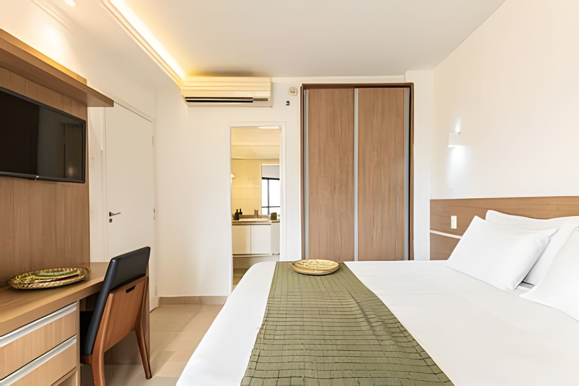 Una habitación de hotel con cama, escritorio, silla, televisor y armario.