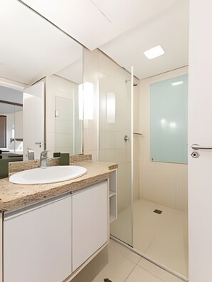 Une salle de bain moderne avec une douche à l’italienne en verre, un lavabo blanc et un grand miroir.