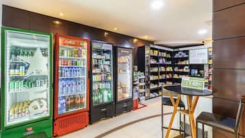 A convenience store with refrigerated beverage dispensers, shelves stocked with snacks and drinks, and a small seating area with a table and chairs.