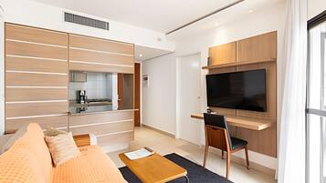 A modern living room with a sofa, coffee table, TV, and a kitchen area in the background.