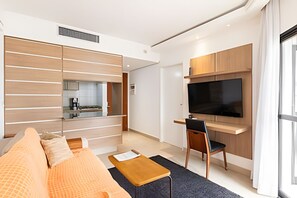 Een moderne woonkamer met een bank, salontafel, televisie en een keuken op de achtergrond.