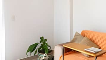 A minimalist room with a bed, a small table, a plant, and a pet bed.