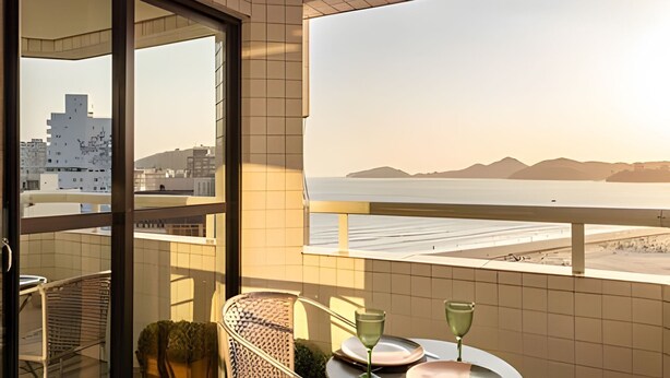 A balcony with a view of the sea and mountains, a table with plates and glasses, and a chair. - ARK Houses - Flat Standard Vista-Mar c/ Piscina na Cobertura (Santos)