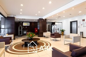Een moderne lobby met een centrale salontafel, een zithoek en een receptiebalie.