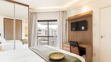 A hotel room with a bed, a desk, a television, and a view of the cityscape.