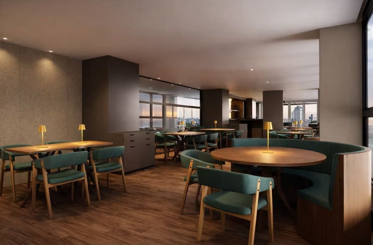 Un comedor moderno con mesas de madera y sillas tapizadas de verde, amplias ventanas con vista a la ciudad y una zona de cocina con vistas.