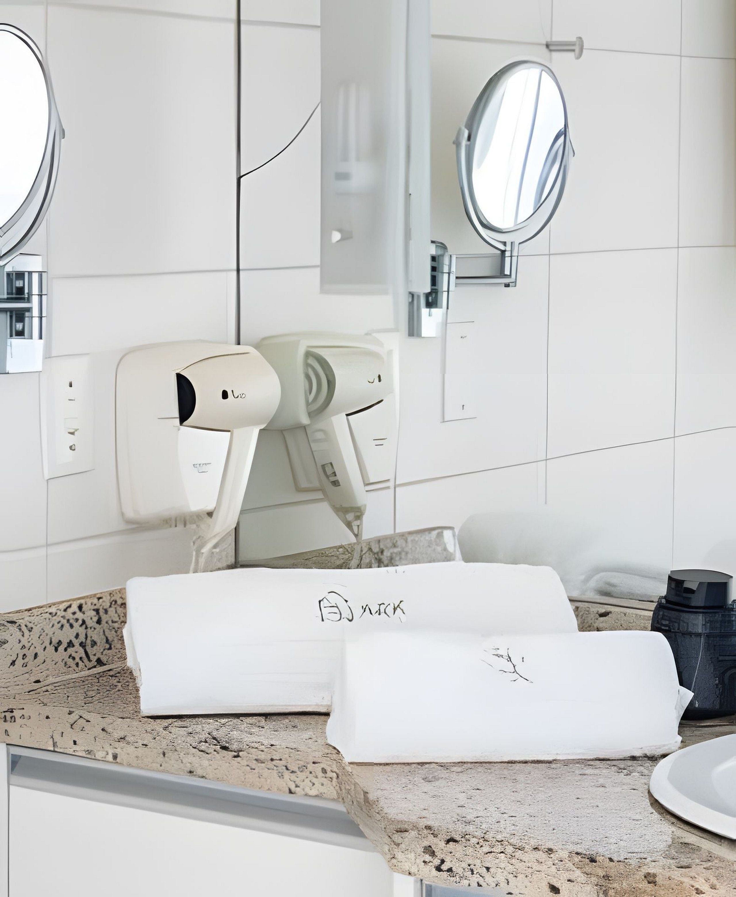 A bathroom with a white countertop, two hair dryers, a towel rack, and a mirror.
