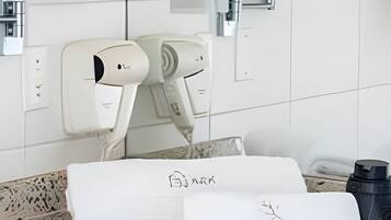 A bathroom with a white countertop, two hair dryers, a towel rack, and a mirror.