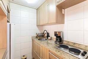 Een kleine keuken met een spoelbak, koffiezetapparaat en twee inductiekookplaten.