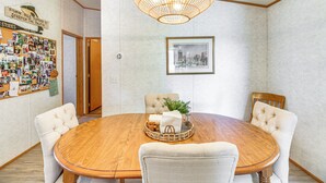 Ein Esszimmer mit einem runden Holztisch, gepolsterten Stühlen, einer Pendelleuchte, einem gerahmten Bild an der Wand und einem Korkbrett mit angehefteten Gegenständen.