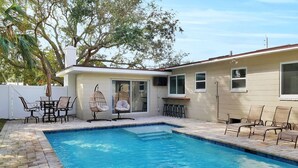 A swimming pool with a tiled deck, outdoor seating, and a building with large windows. - 3-bedroom House with Heated Pool in Delightful St. Augustine. Pet-Friendly! (St. Augustine)