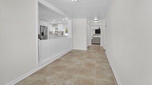 A hallway with a kitchen area visible in the distance, featuring white walls and tiled flooring. - 3-bedroom House with Heated Pool in Delightful St. Augustine. Pet-Friendly! (St. Augustine)