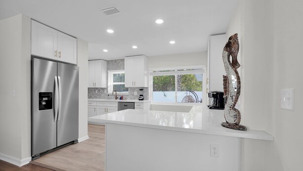 A modern kitchen with a stainless steel refrigerator, white cabinetry, and a large island. - 3-bedroom House with Heated Pool in Delightful St. Augustine. Pet-Friendly! (St. Augustine)