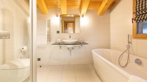 Un baño moderno con cabina de ducha de vidrio, bañera independiente y tocador con lavabo y espejo.