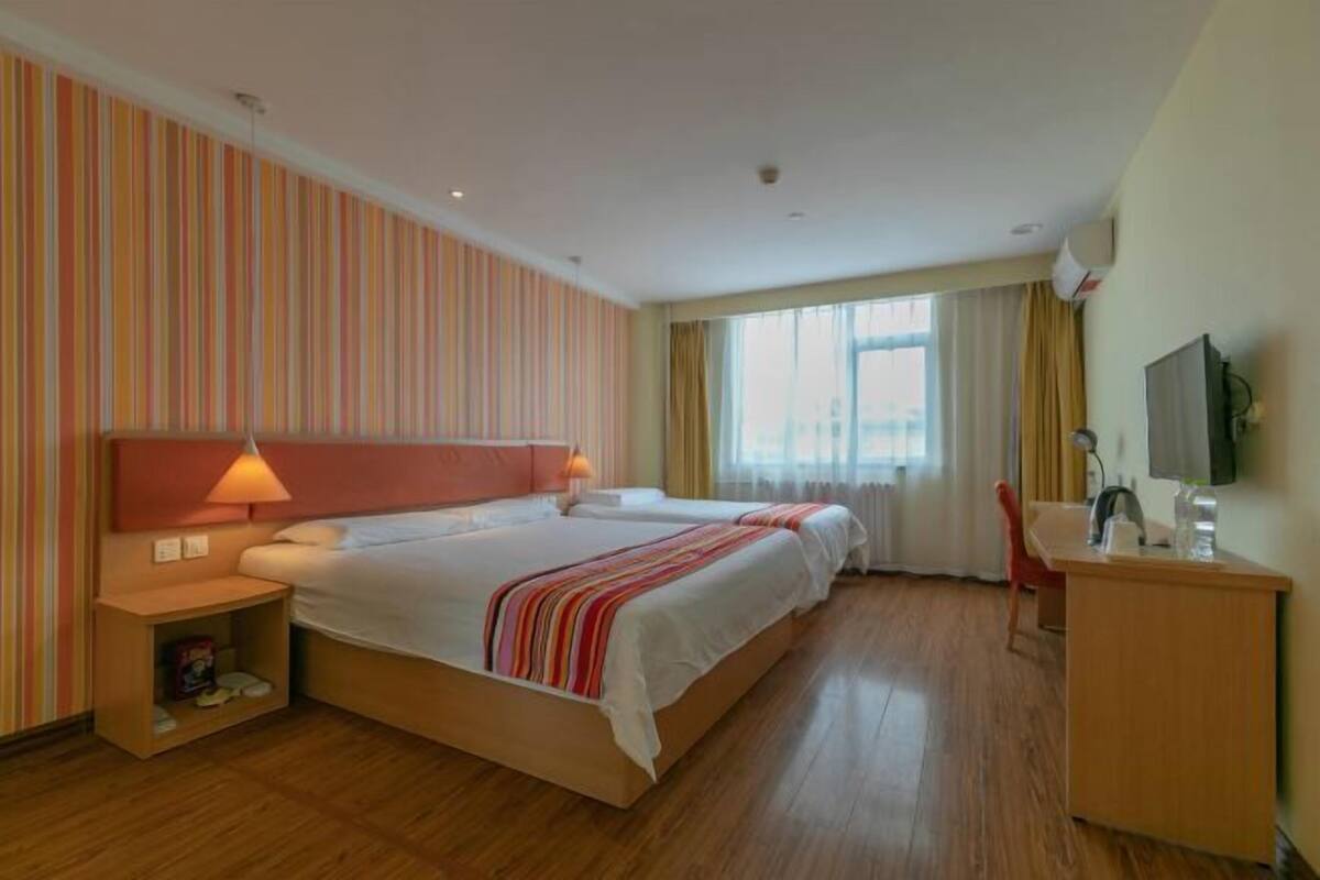 A hotel room with a large bed, bedside tables, a desk, and a television.