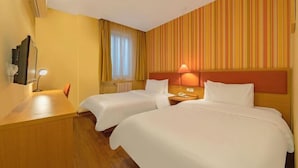 Een hotelkamer met twee bedden, een houten bureau, een spiegel, een lamp en een raam met gordijnen.