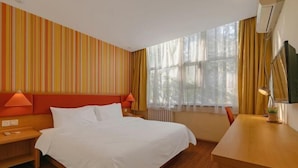 Hotelkamer met een bed, bureau, stoel, nachtkastje, lamp, televisie en raam met gordijnen.
