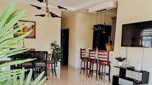 A spacious living room with a sofa set, a dining area with chairs, a TV mounted on the wall, and a ceiling fan. - Beautiful 3BR villa in Ocho Rios near Dunn's River falls, gorg beaches plus more (Ocho Rios)