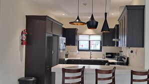 A modern kitchen with dark cabinets, a white island, and pendant lighting. - Beautiful 3BR villa in Ocho Rios near Dunn's River falls, gorg beaches plus more (Ocho Rios)
