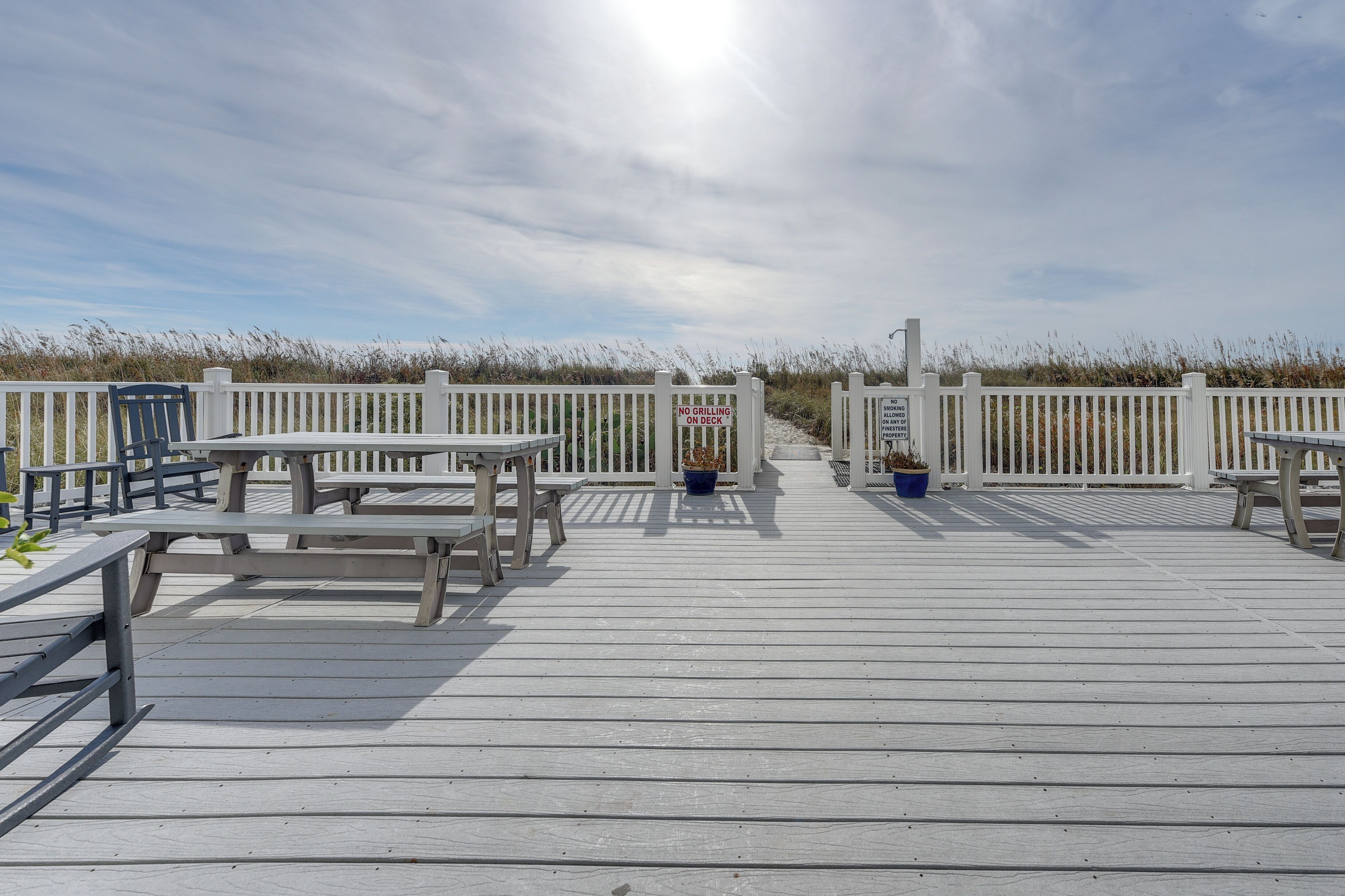 A wooden deck with picnic tables and benches, a white picket fence, and a sign prohibiting grilling.