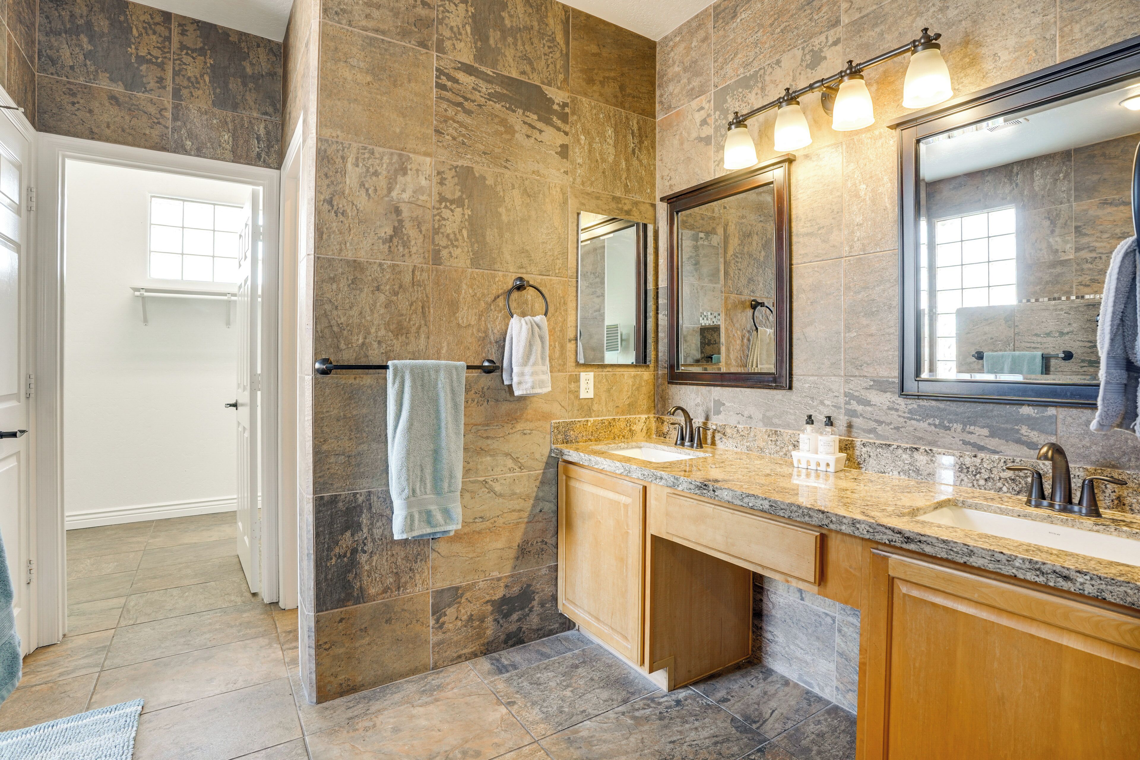 A modern bathroom with a large mirror, granite countertops, and a walk-in shower.