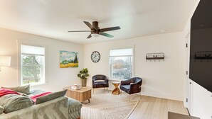 Un salón amplio con un gran ventanal, ventilador de techo, sofá, dos sillones, una mesa de centro y televisor.