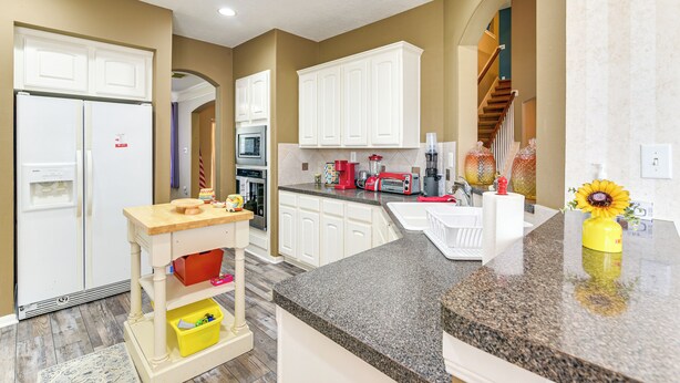 A kitchen with white cabinets, a granite countertop, and a yellow vase with a sunflower.