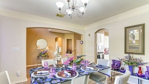 A dining area with a table set for two, chairs, a chandelier, and a vase with flowers.