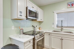 A kitchen with white cabinets, a microwave, stove, oven, and a window with blinds.