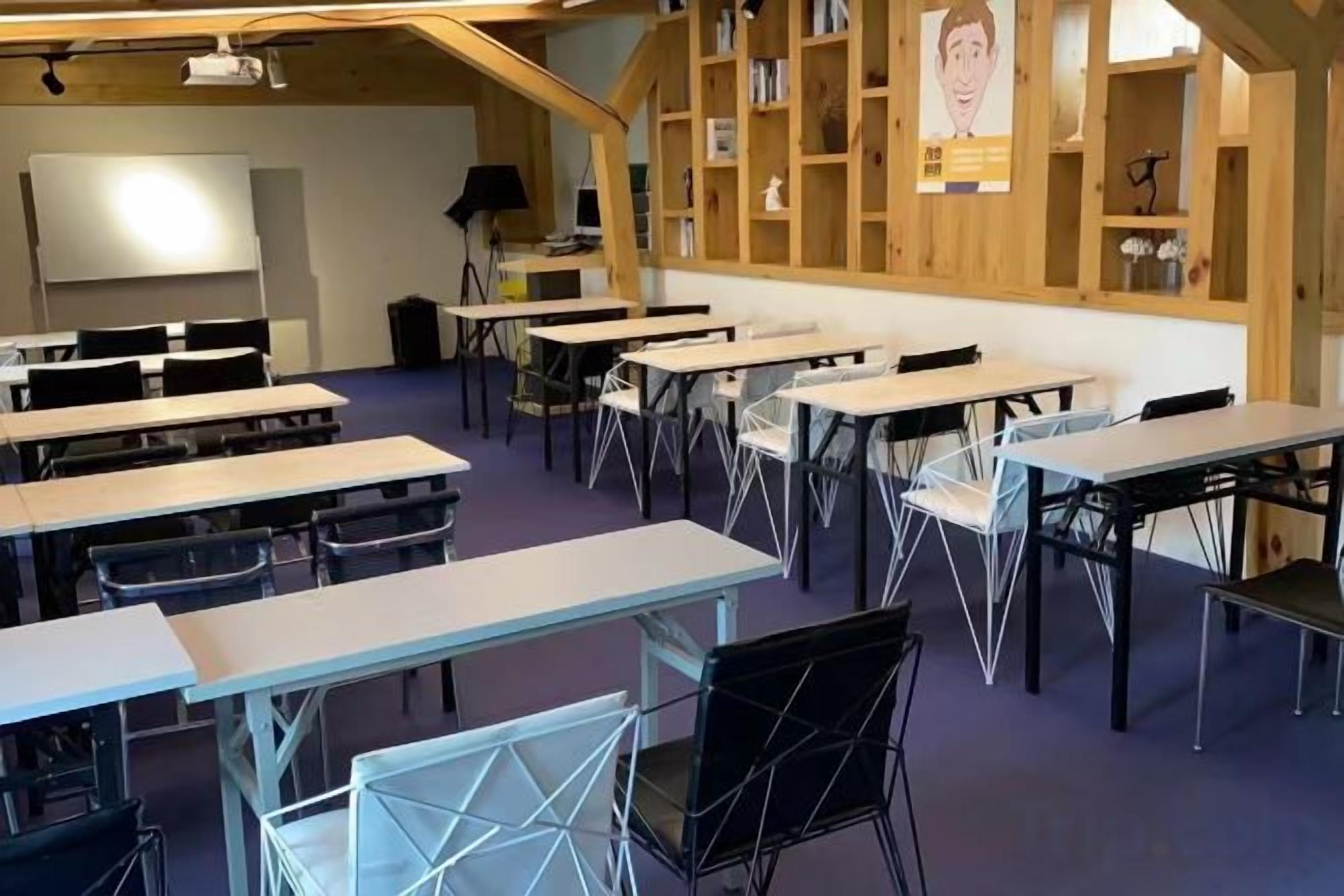 Un aula con mesas y sillas, estanterías de madera y una pantalla de proyector.