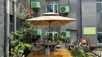 An outdoor patio with a table and chairs, surrounded by potted plants and a large umbrella.