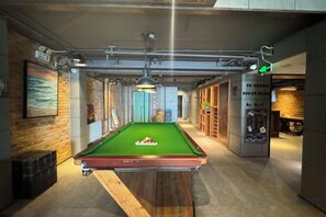 A pool table in a room with a wooden floor, a brick wall, and a hanging light fixture. - In Hotels (Qingdao)