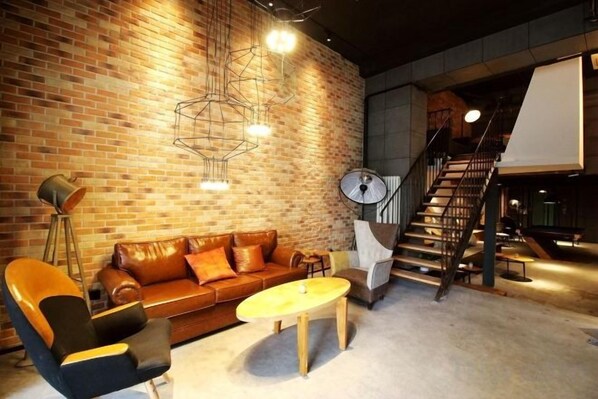 A furnished room with a brick wall, a sofa, a coffee table, a chair, a lamp, and a staircase.