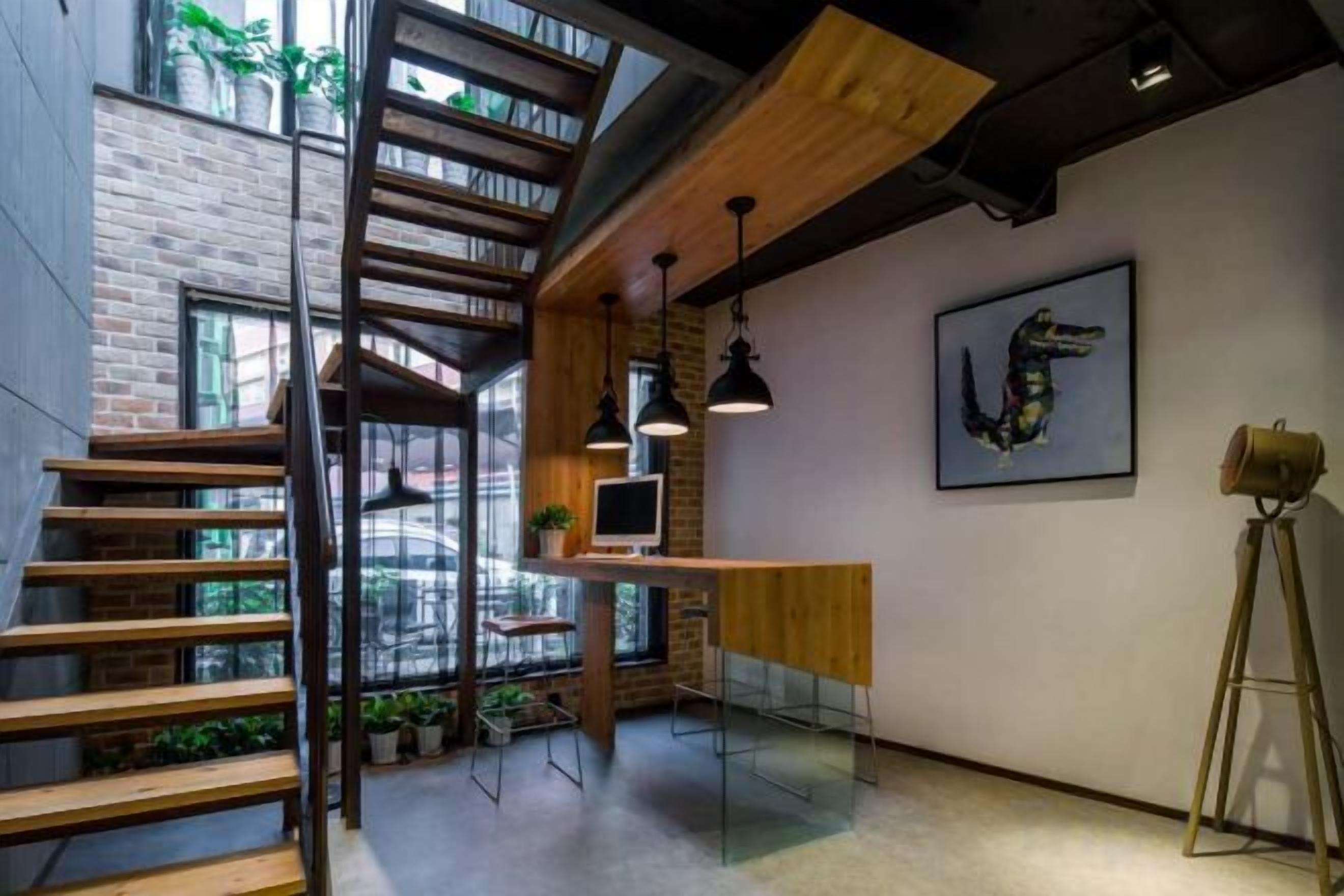 Un interior moderno con una escalera de madera, un escritorio con una computadora y una obra de arte enmarcada en la pared.