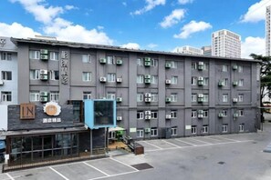 A multi-story building with a row of windows on each floor, a parking lot in front, and a sign with a logo and text.